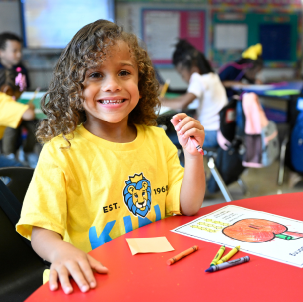 A person smiles while sitting at a table with crayons