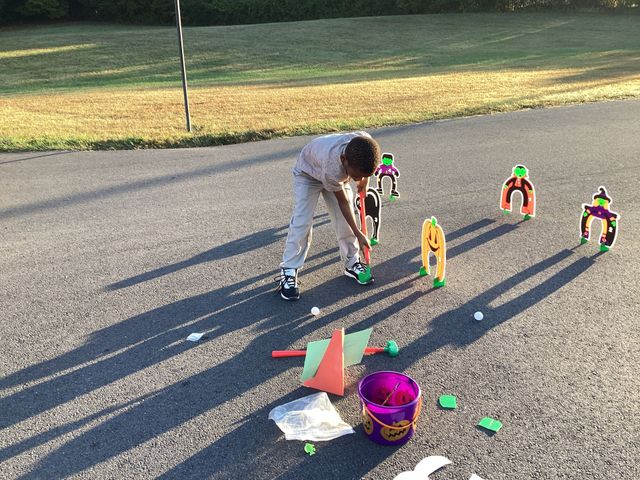 The image shows a young person playing with toys on the street, surrounded by colorful play items.
