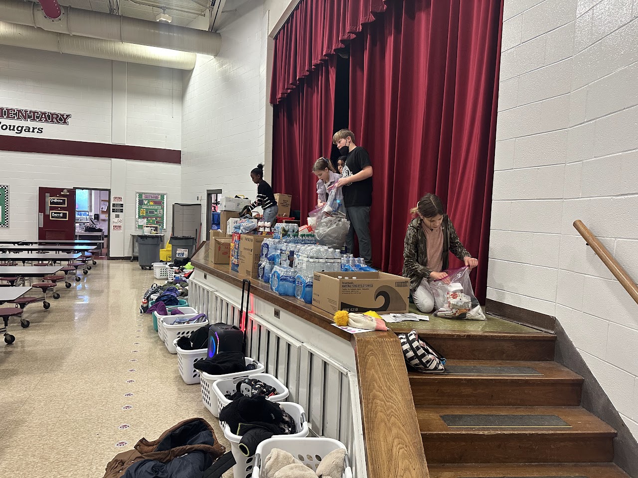 Volunteers helping to load boxes with donations at a school event in the gymnasium.