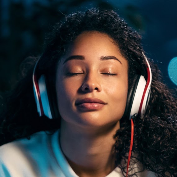 A person with closed eyes, wearing headphones and appearing relaxed or meditative.