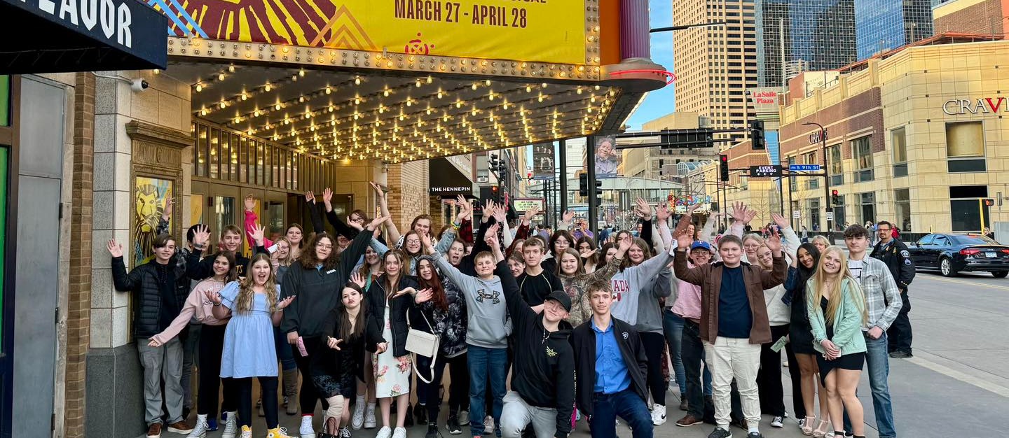 Students stand posing under a marquee prior to the performance of The Lion King in the Twin Cities.