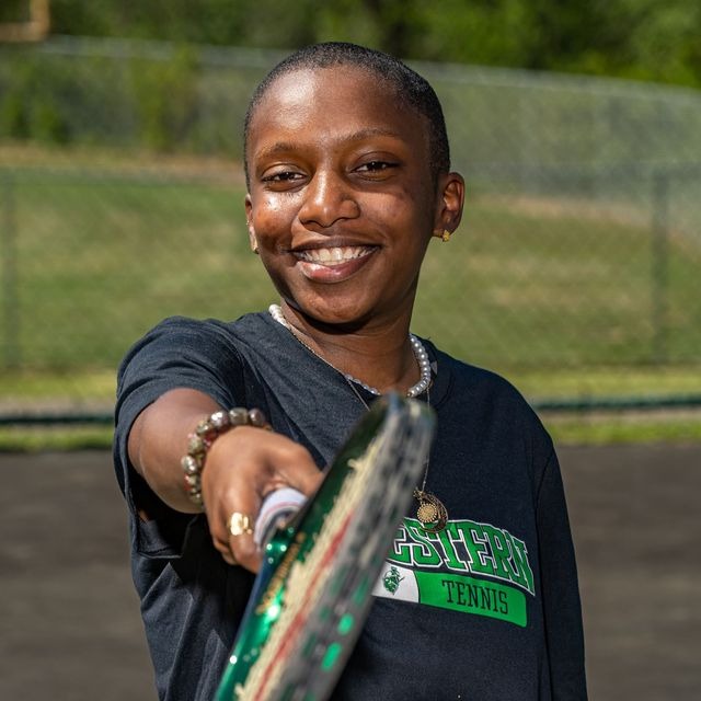 student holding tennis racked facing/pointing at the camera