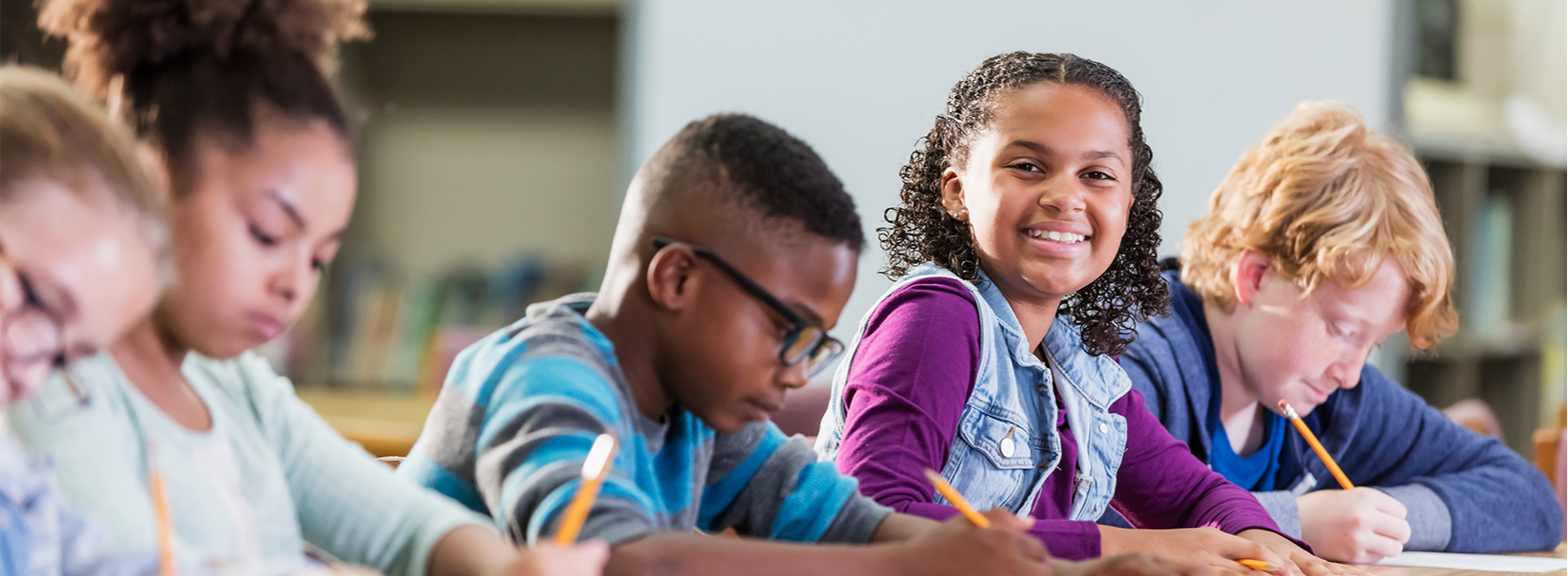 Students working on paper and girl looking at a camera smiling