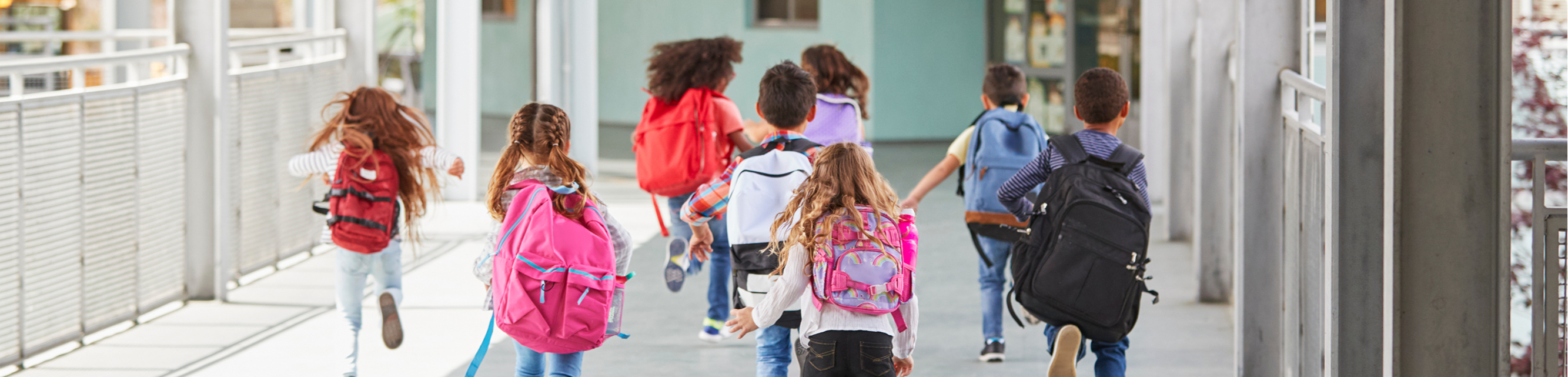 Group of kids running through a school hall wearing backpacks