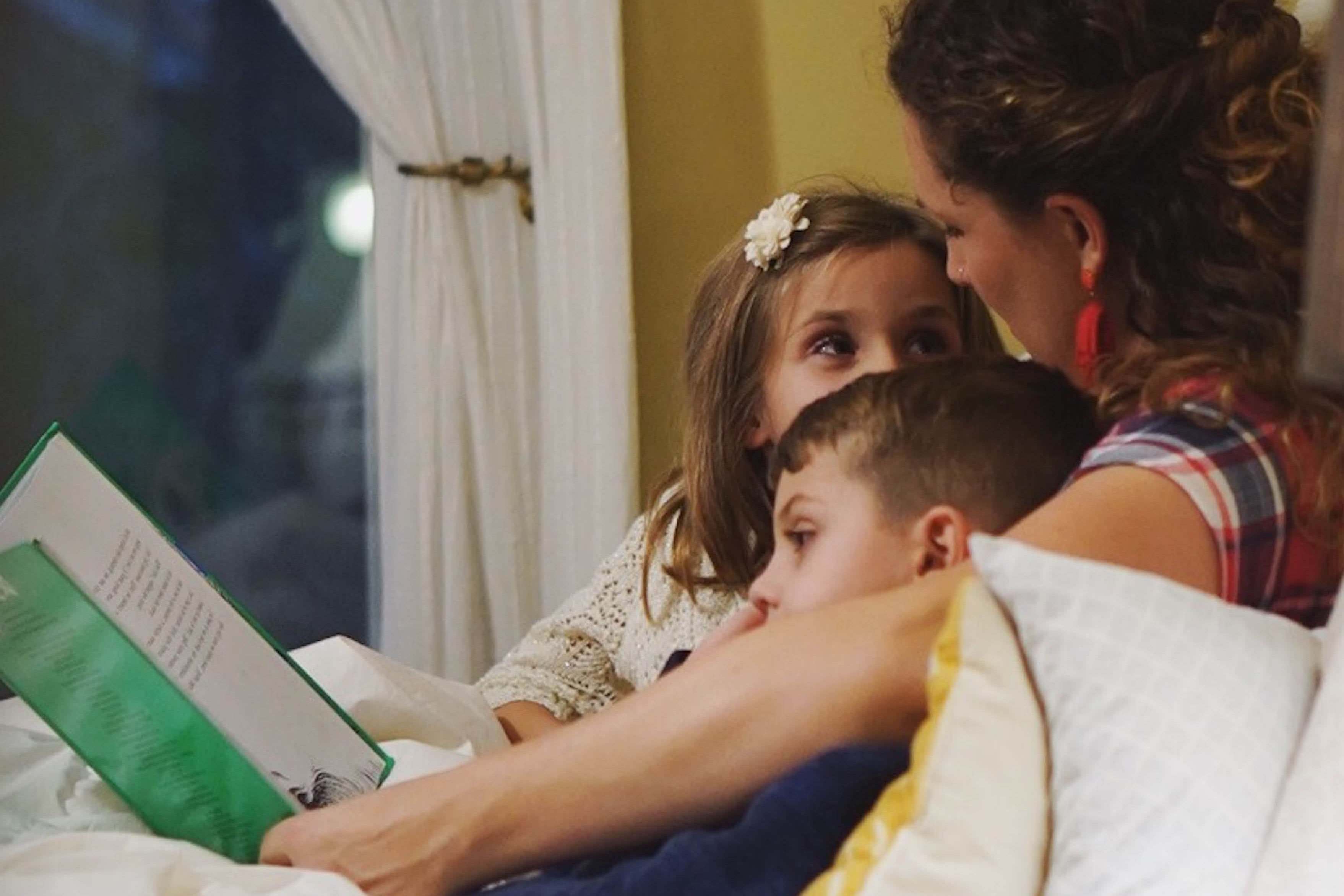 Mom with two kids reading a green covered book in bed