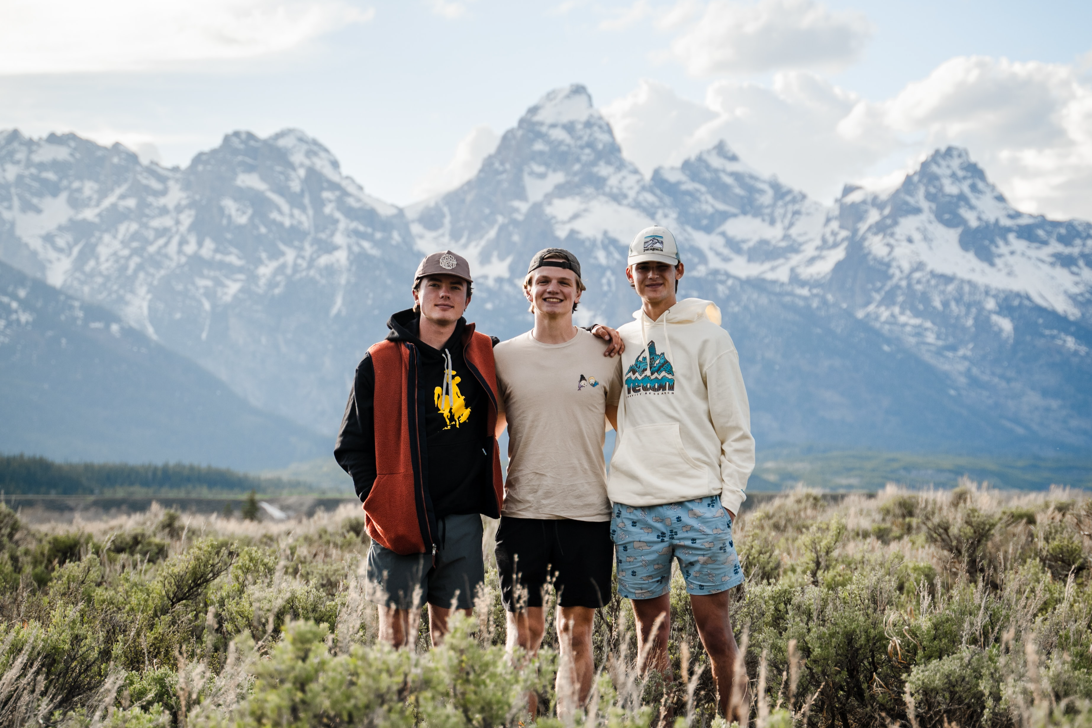 Three young adult males in a field in front of the Grand Teton Mountains