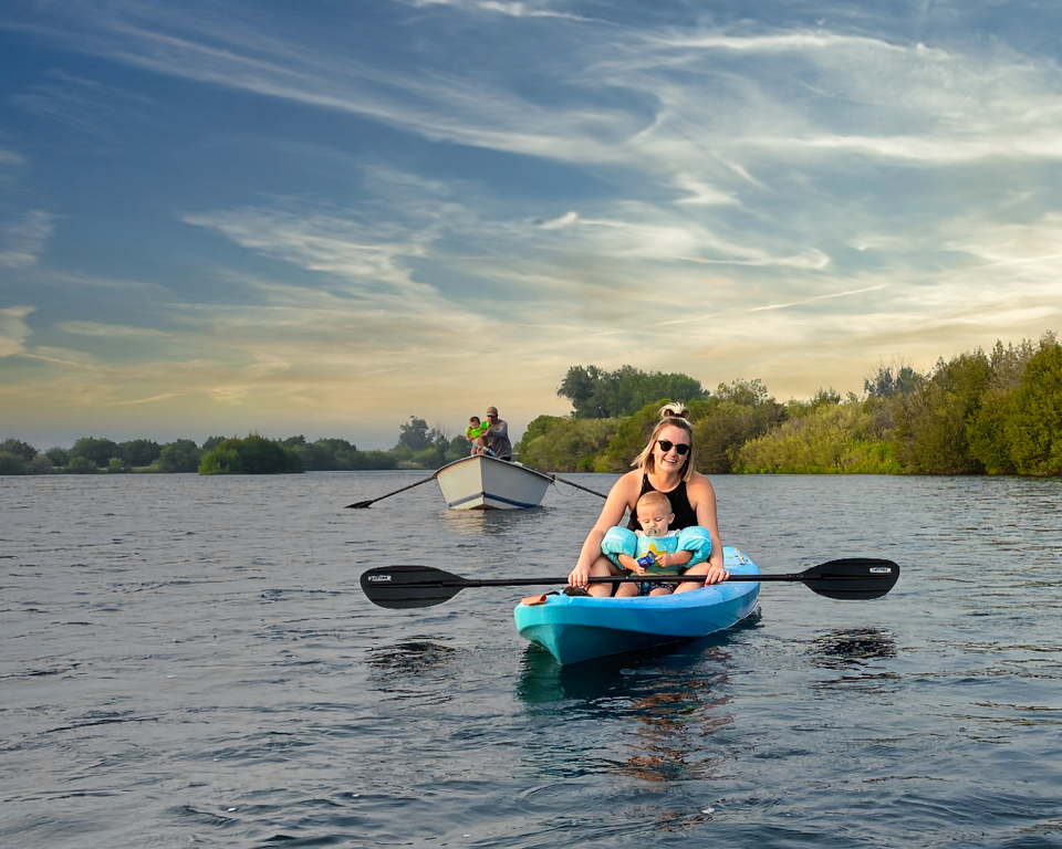 woman kayaking on the river with a canoe not far behind her