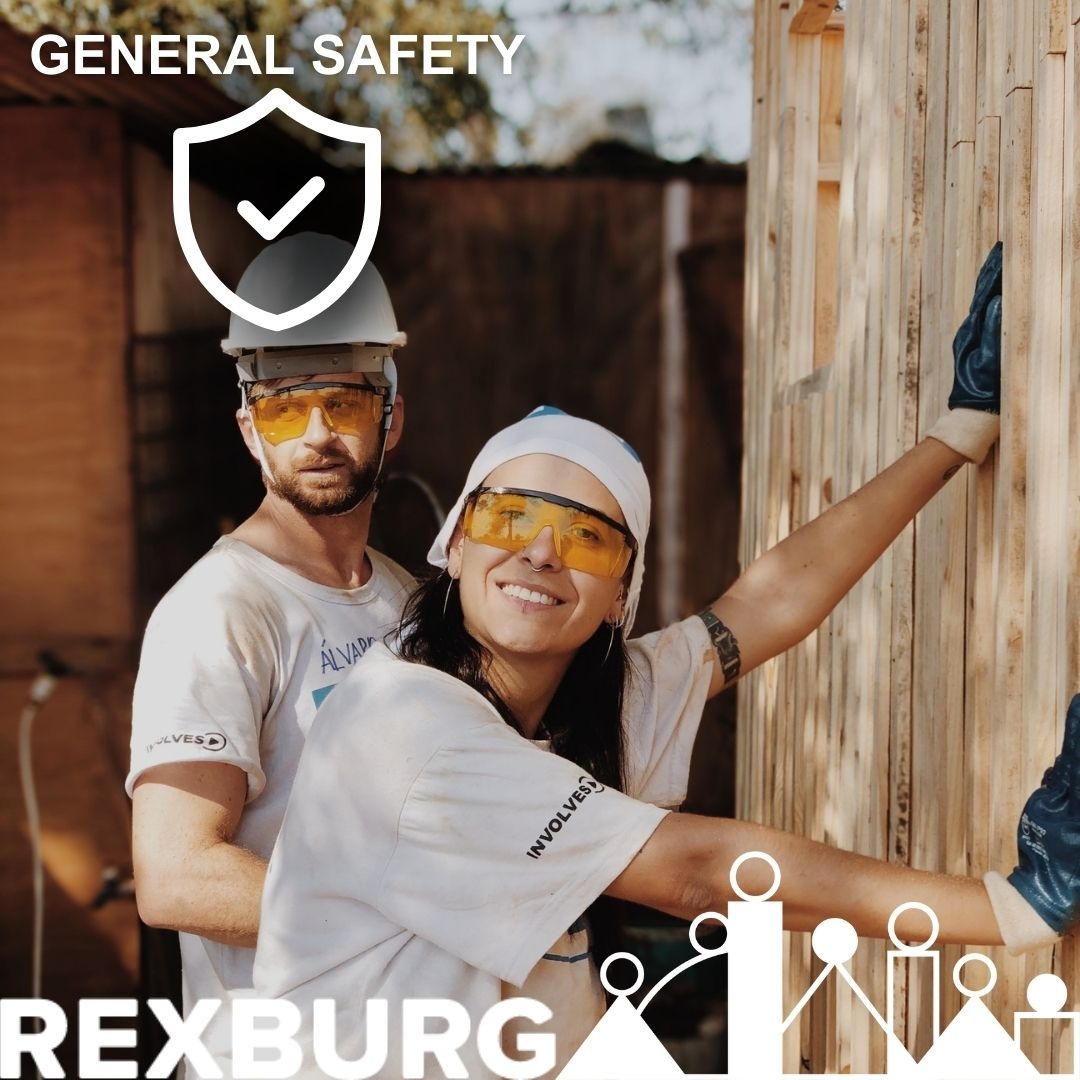 Two adults with safety hats and glasses on working outside holding up a wood platform