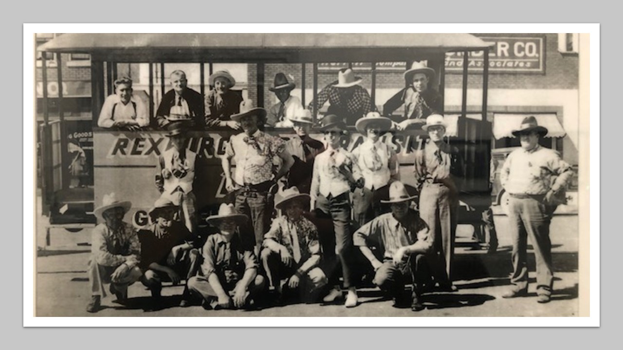 Historic photo of multiple adults gathered in and in front of a trolley on Main Street in Rexburg