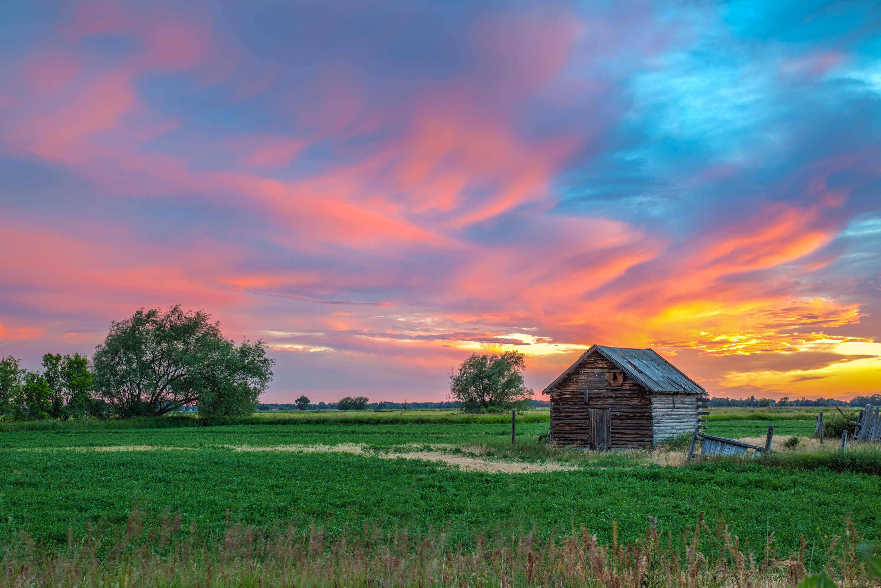 sunset over a small old rustic log shed in a green field