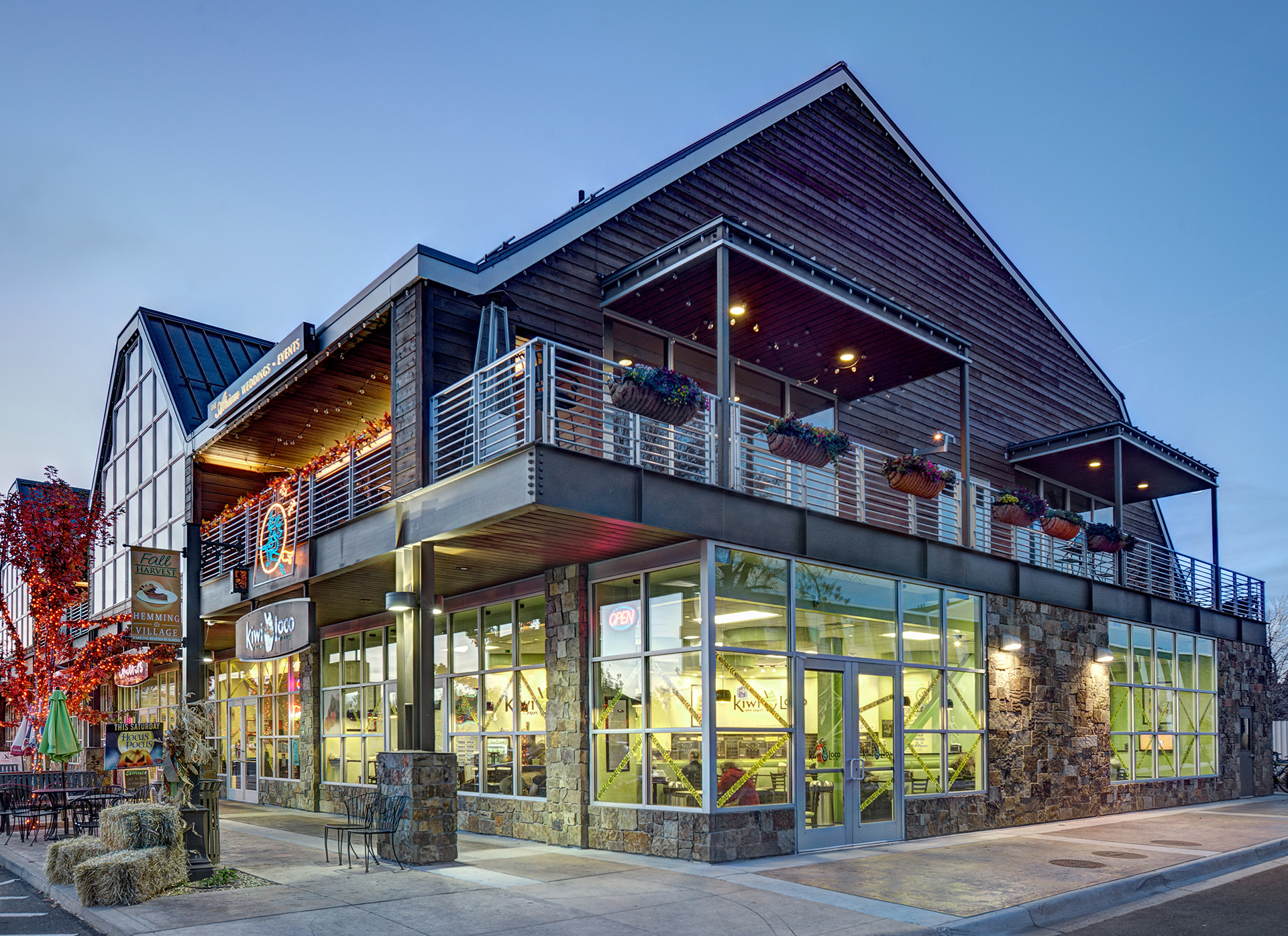dusk photo of window-framed shopping center at Hemming Village, decked out for fall with red leaf garland, haybales, and lights