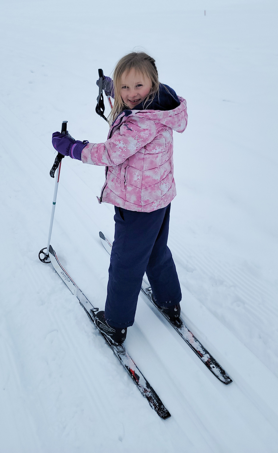 Photo looks down towards a young girl in winter gear on skis on the snow