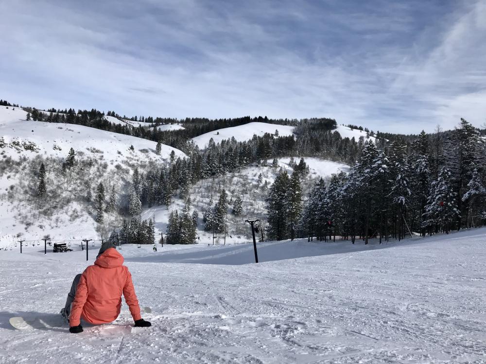 Man on a snowboard facing the snow-covered slope in front of him