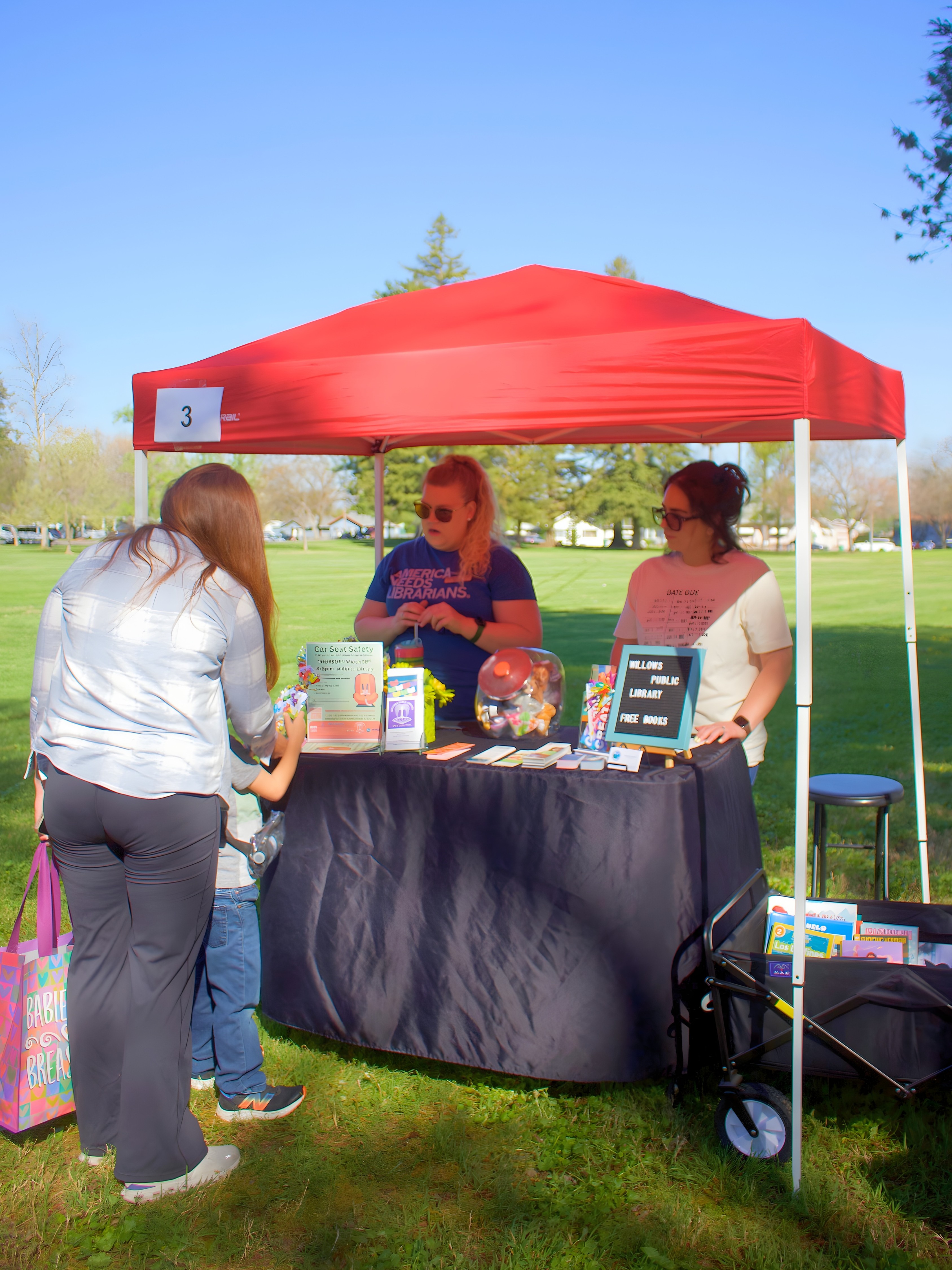 Two adult females assisting child at table with red canopy