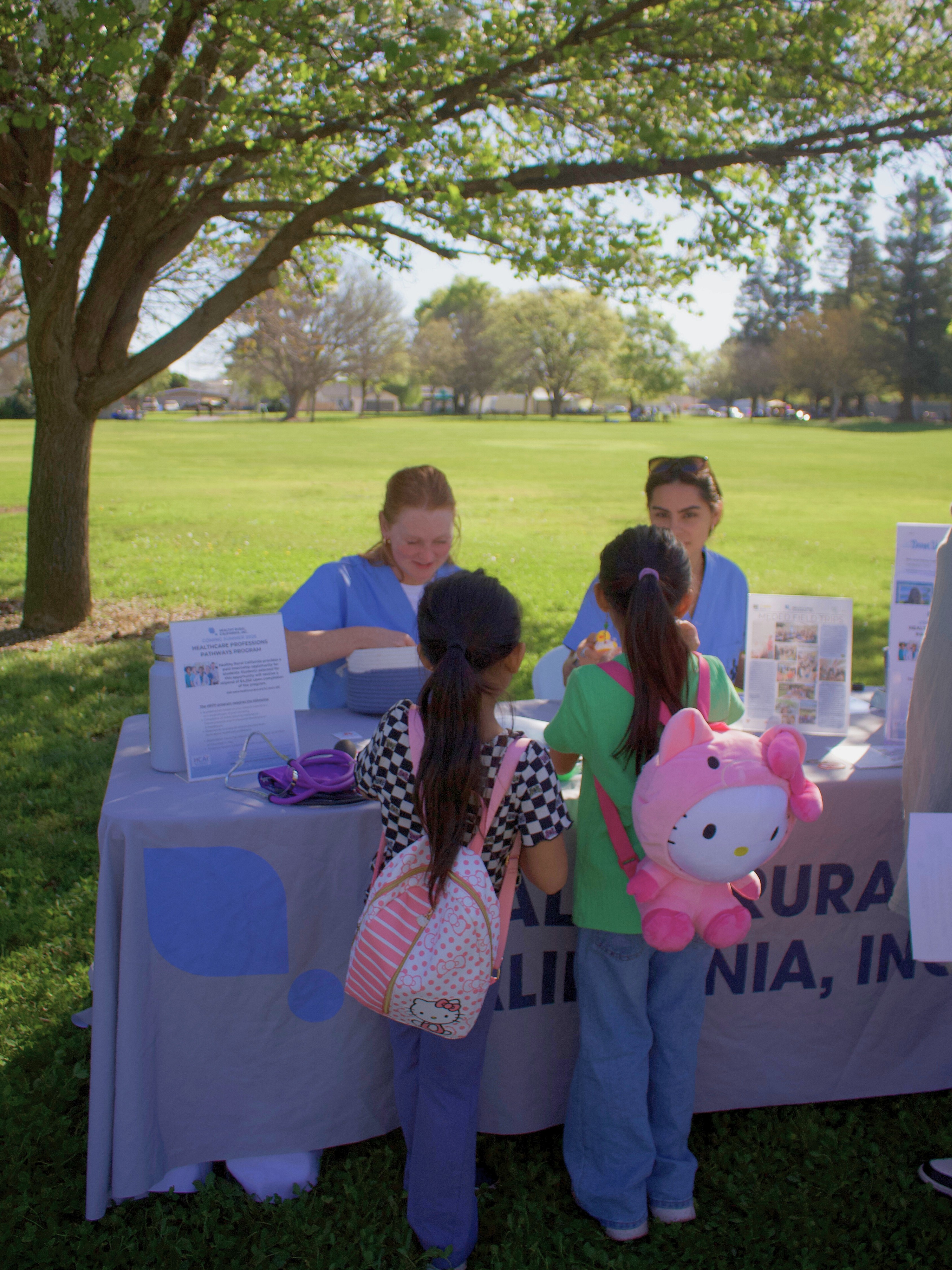 Two female adults sitting at table smiling at two children wearing backpacks