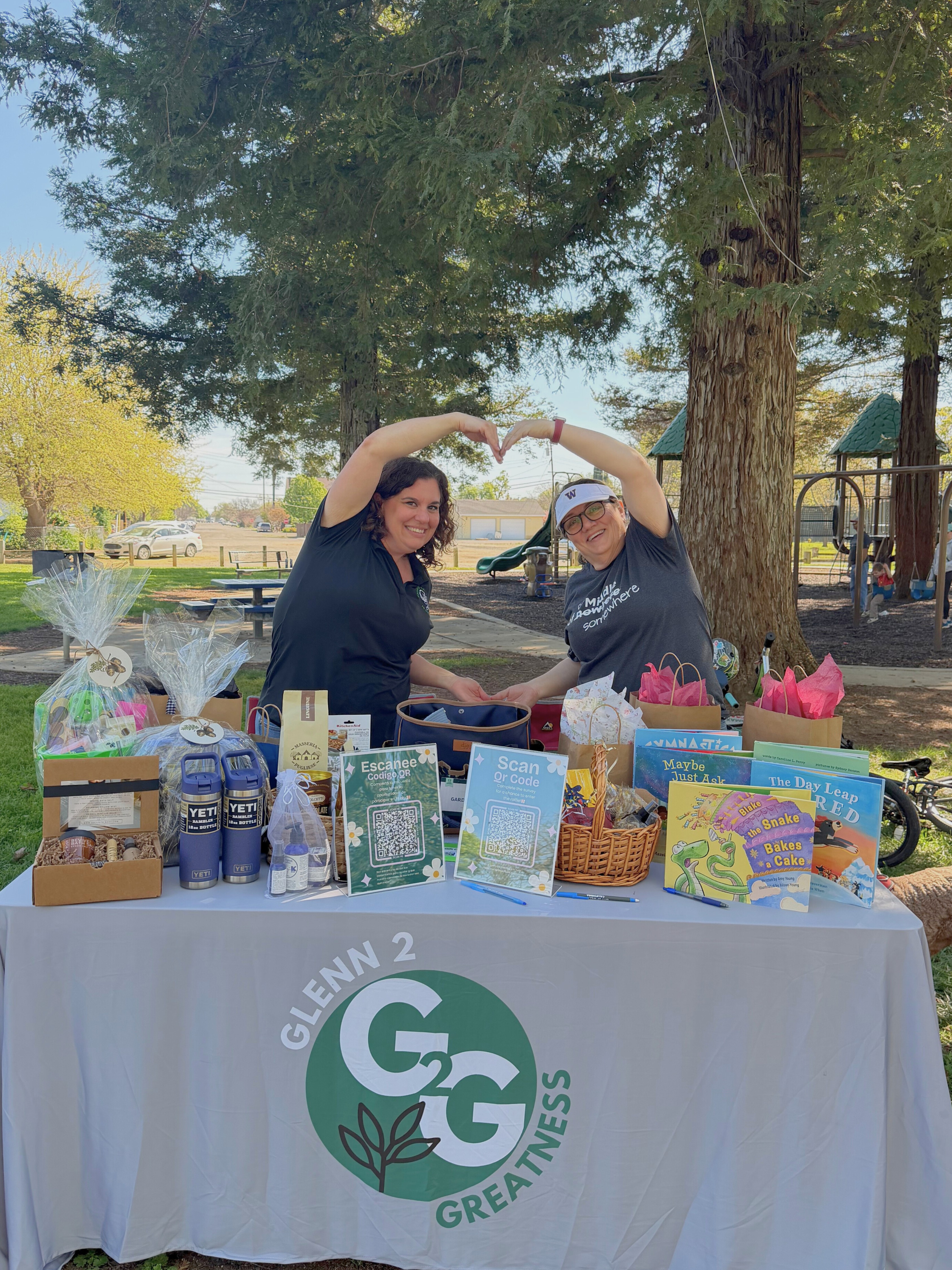 Two females making heart connected with arms at table of books