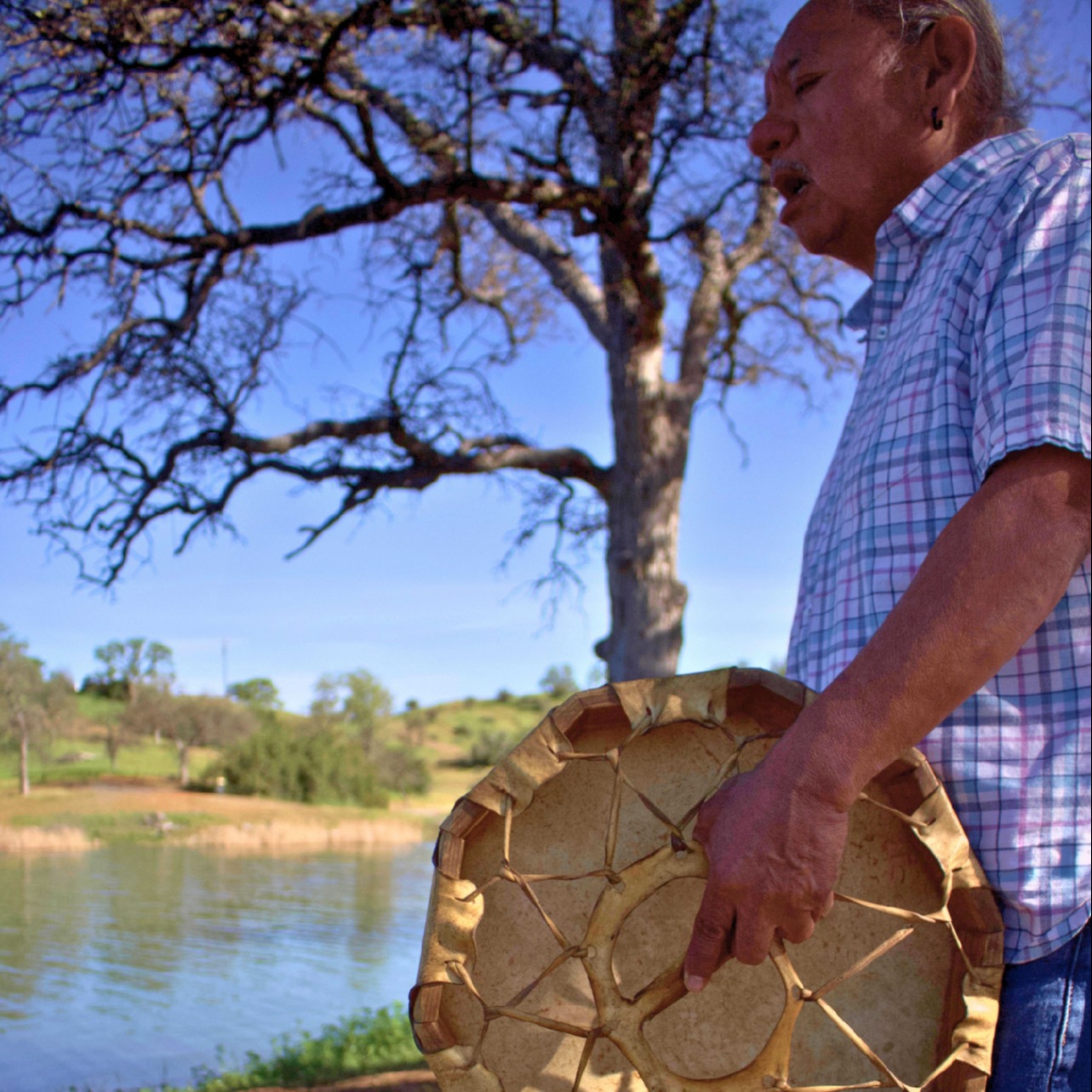 Man with native drum and reservoir in background