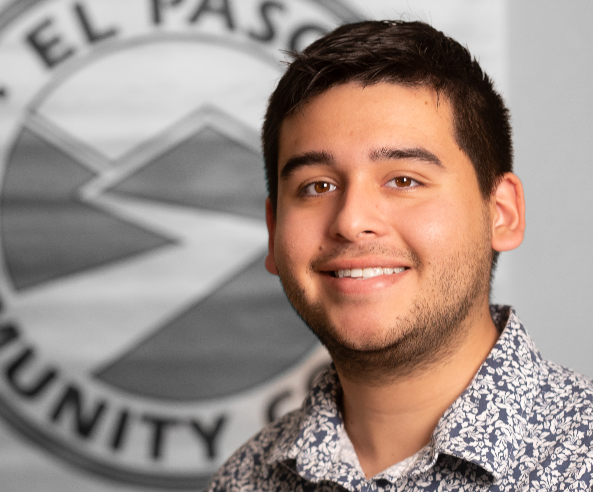 Christian Kelley, Parent Engagement Liaison stands in front of the EPCC logo, he has black hair and is posing.