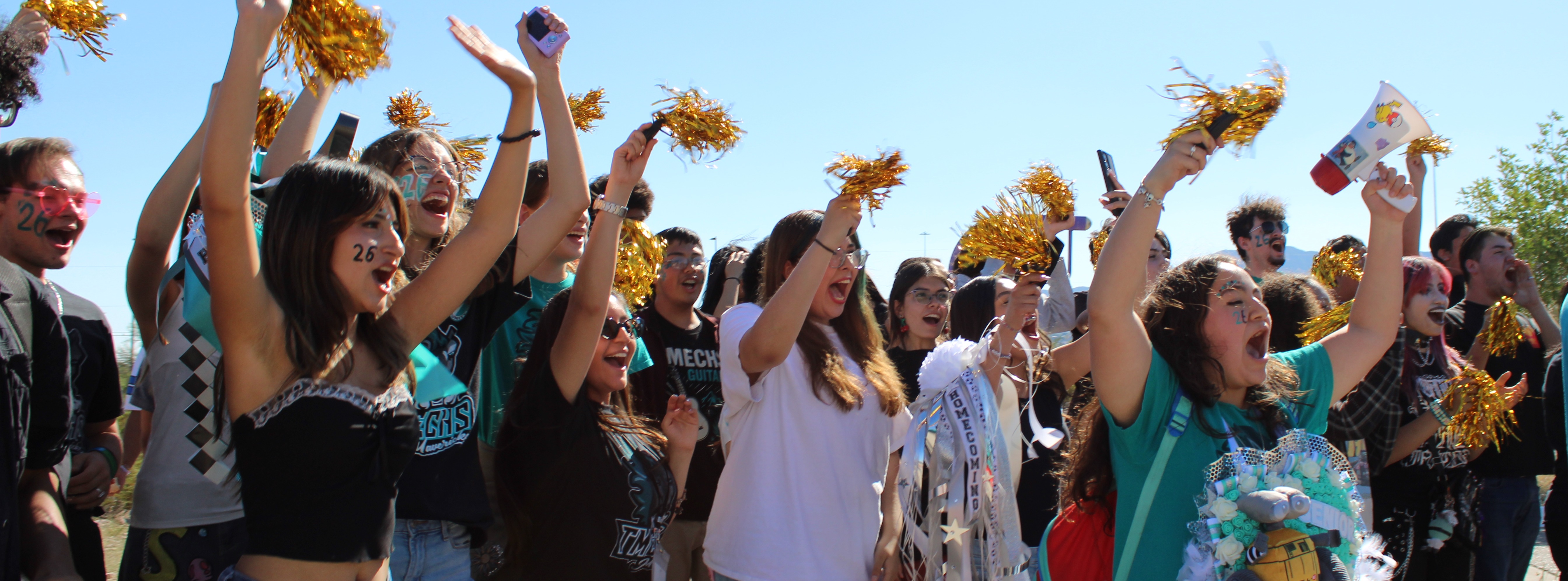 Group of people at a rally with blue sky background, holding pom-poms and cheering.