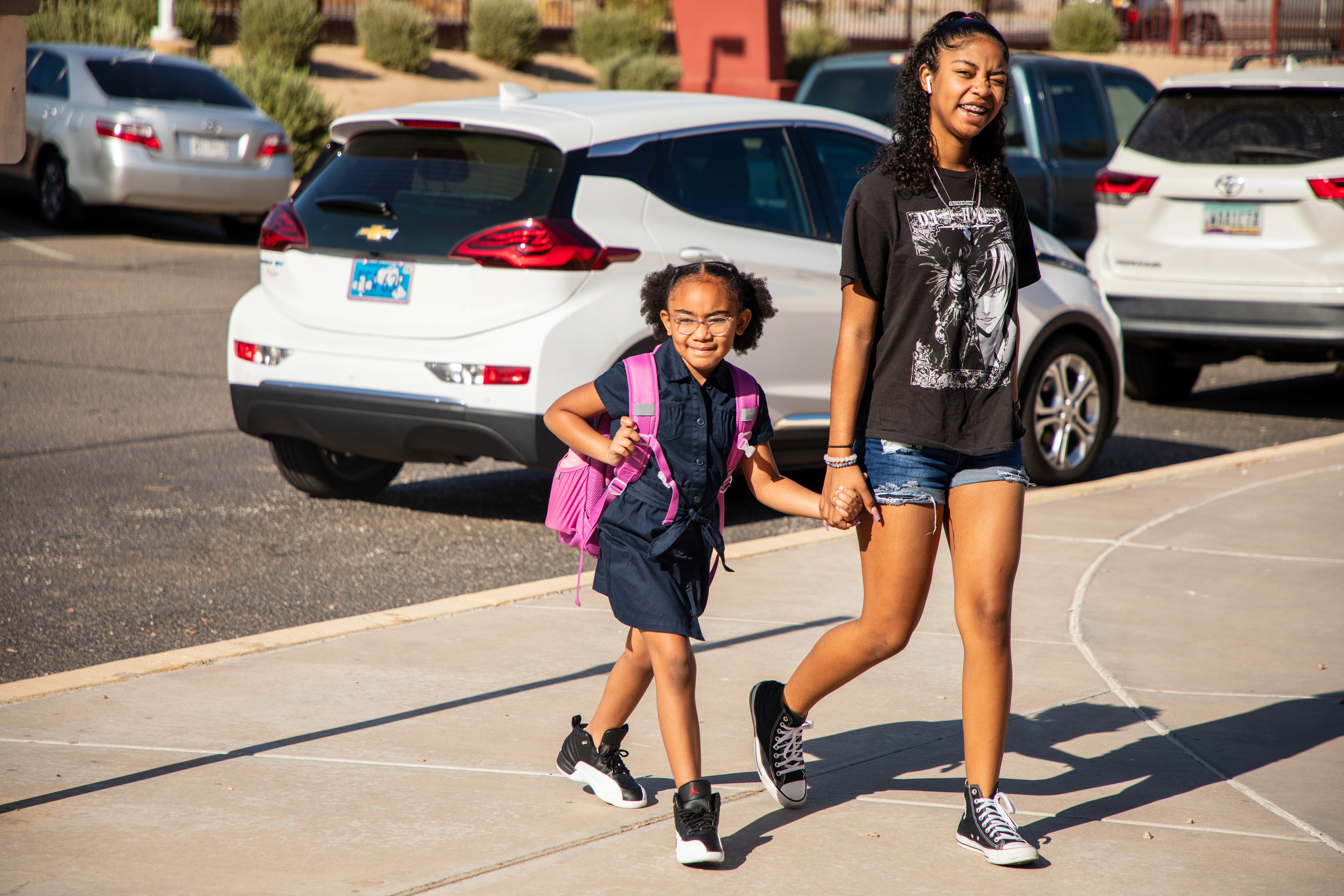 A young female student wearing a navy shirt and skirt being led by the hand by an older relative into school