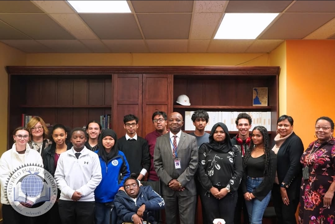 Group photo of students and adults standing together indoors in front of bookshelves. The group appears posed for a school or district event, and a Buffalo Public Schools logo watermark is visible in the lower left corner.
