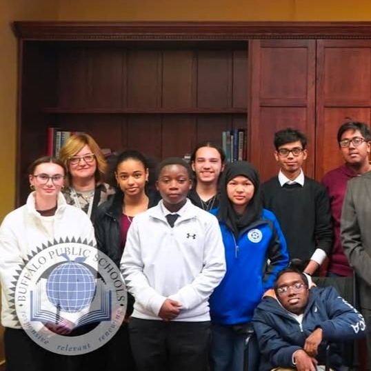 Group photo of students and adults standing together indoors in front of bookshelves. The group appears posed for a school or district event, and a Buffalo Public Schools logo watermark is visible in the lower left corner.