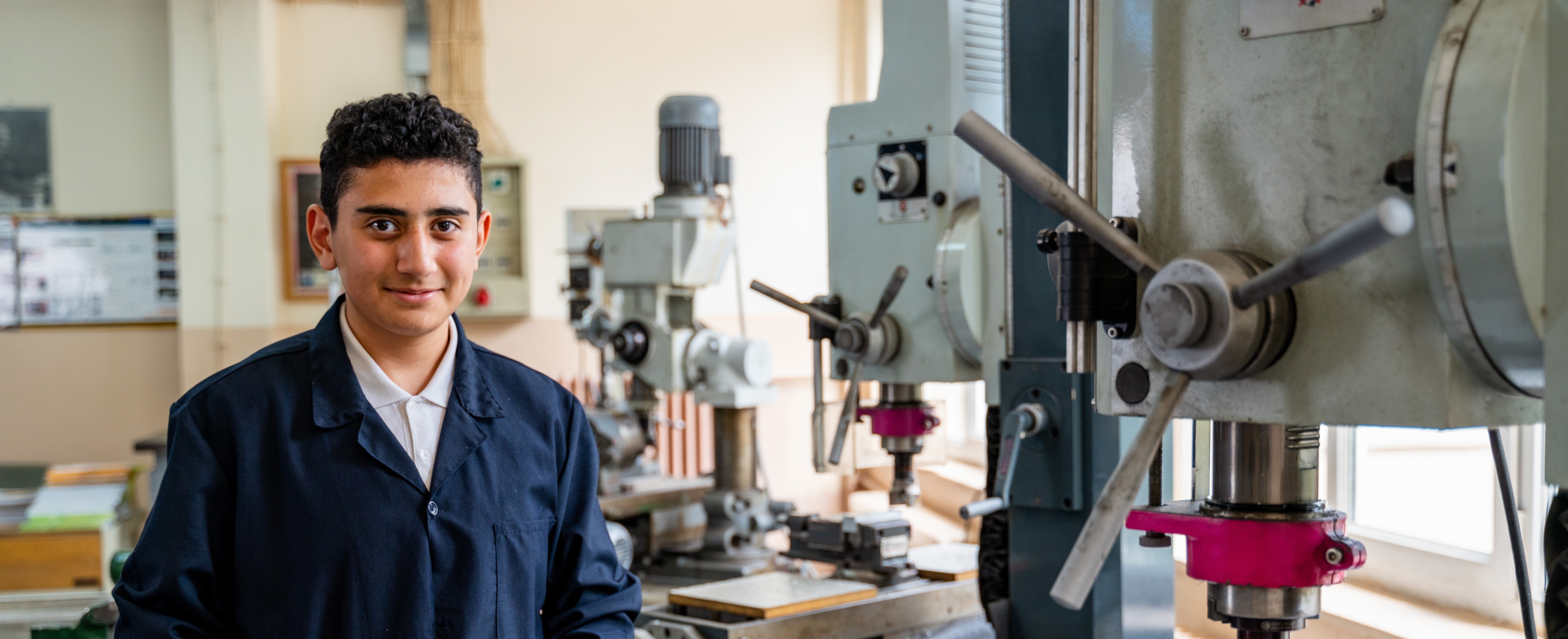 A person stands in front of a workshop machine, proudly showcasing their work environment.
