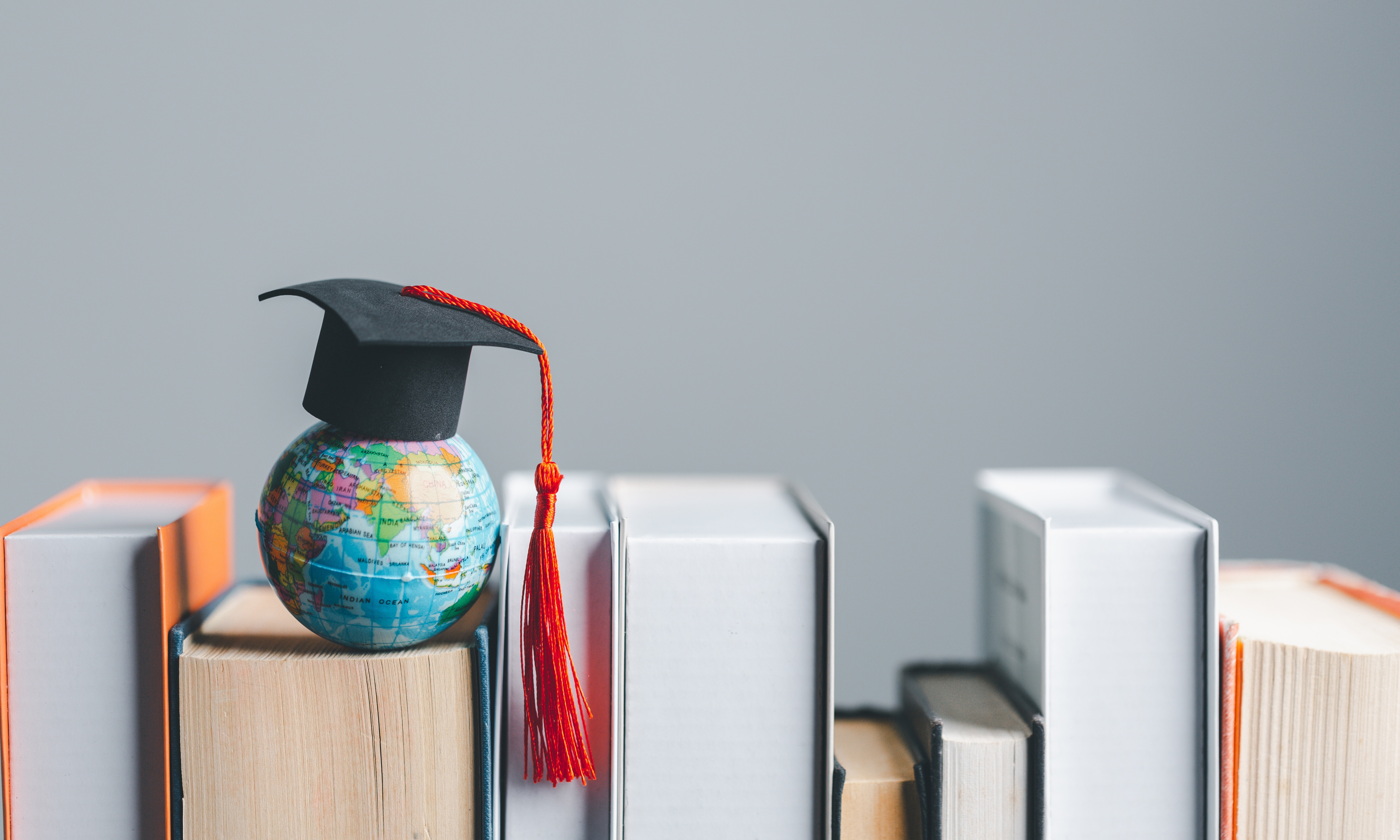 books organized with a small earth globe above them with a graduation hat