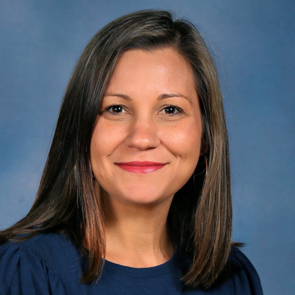 Woman with dark hair and a navy shirt smiling against a blue background.