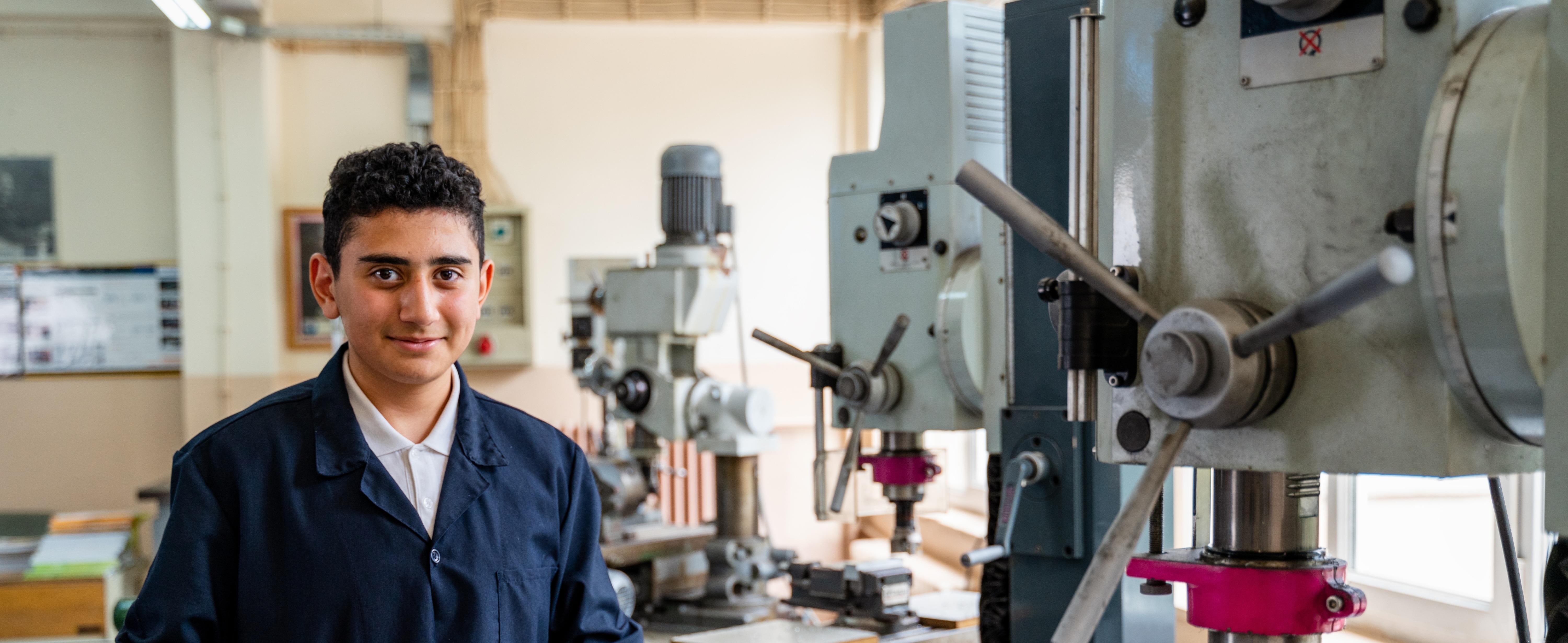 A young person in a lab coat stands proudly by an industrial machine, ready to operate or inspect.