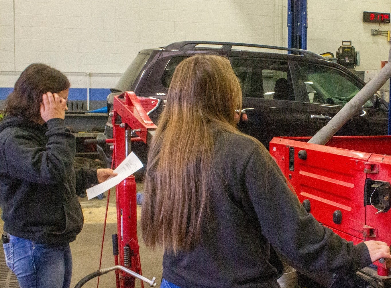 Two individuals in a garage, working on aligning a car with the help of equipment