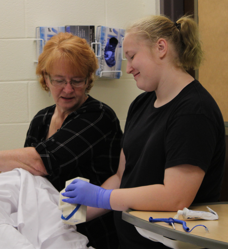 Two individuals are engaged in a medical or care-giving activity involving white sheets or clothing.