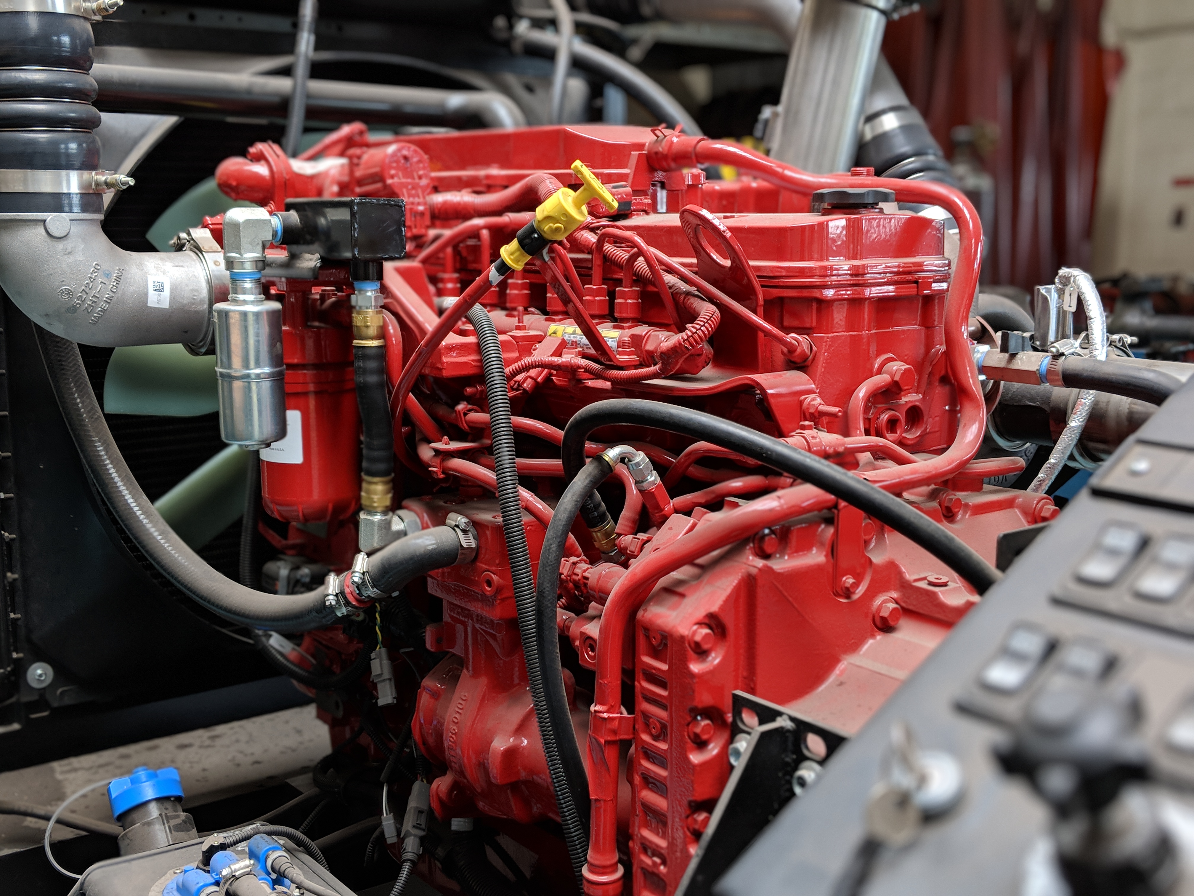 The image shows an engine block is red and there are  silver metal components visible around it.  There are black rubber hoses and  black  tubes connected to the engine block.