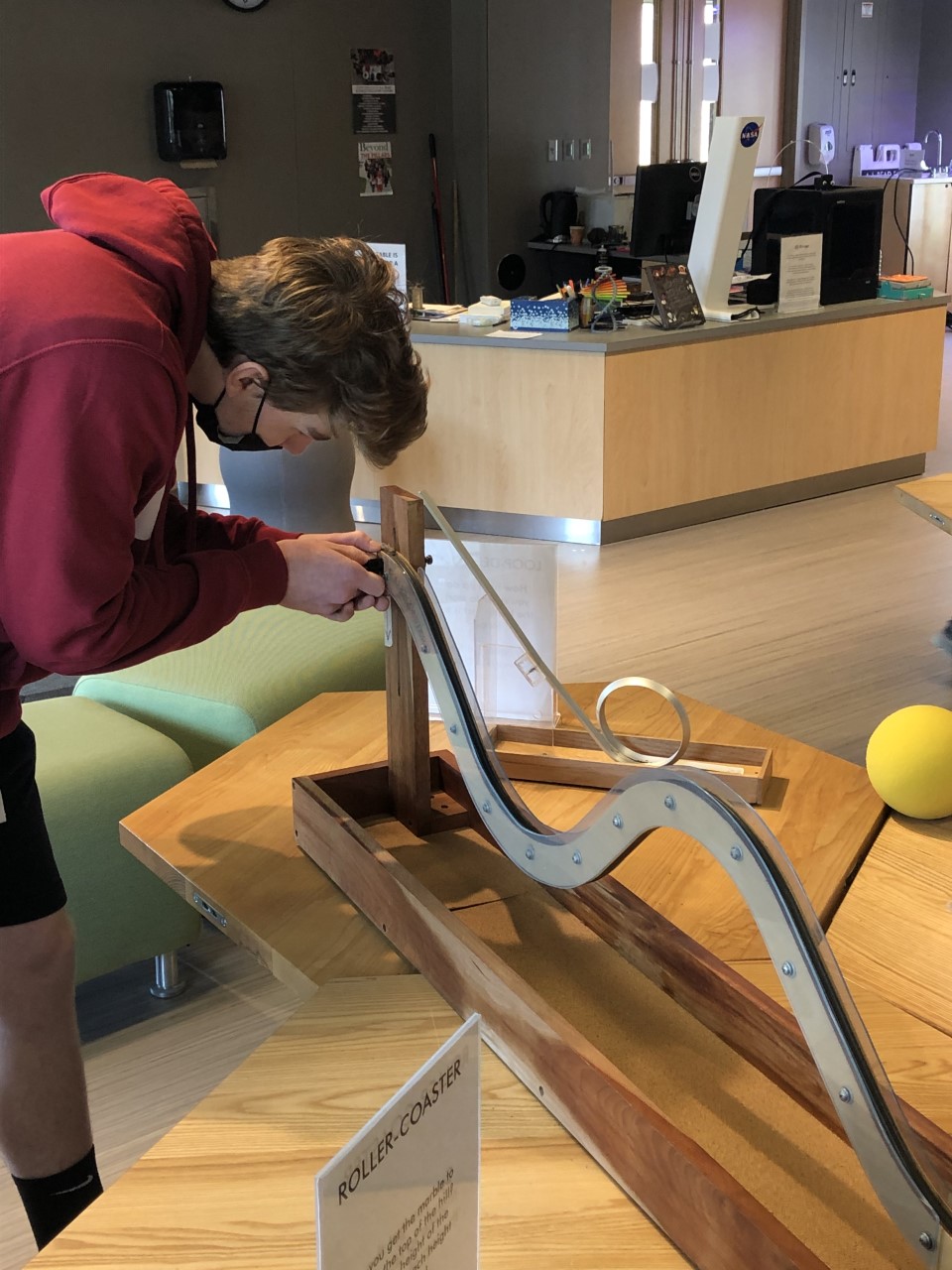 A person is interacting with a wooden and metal roller coaster model on a table