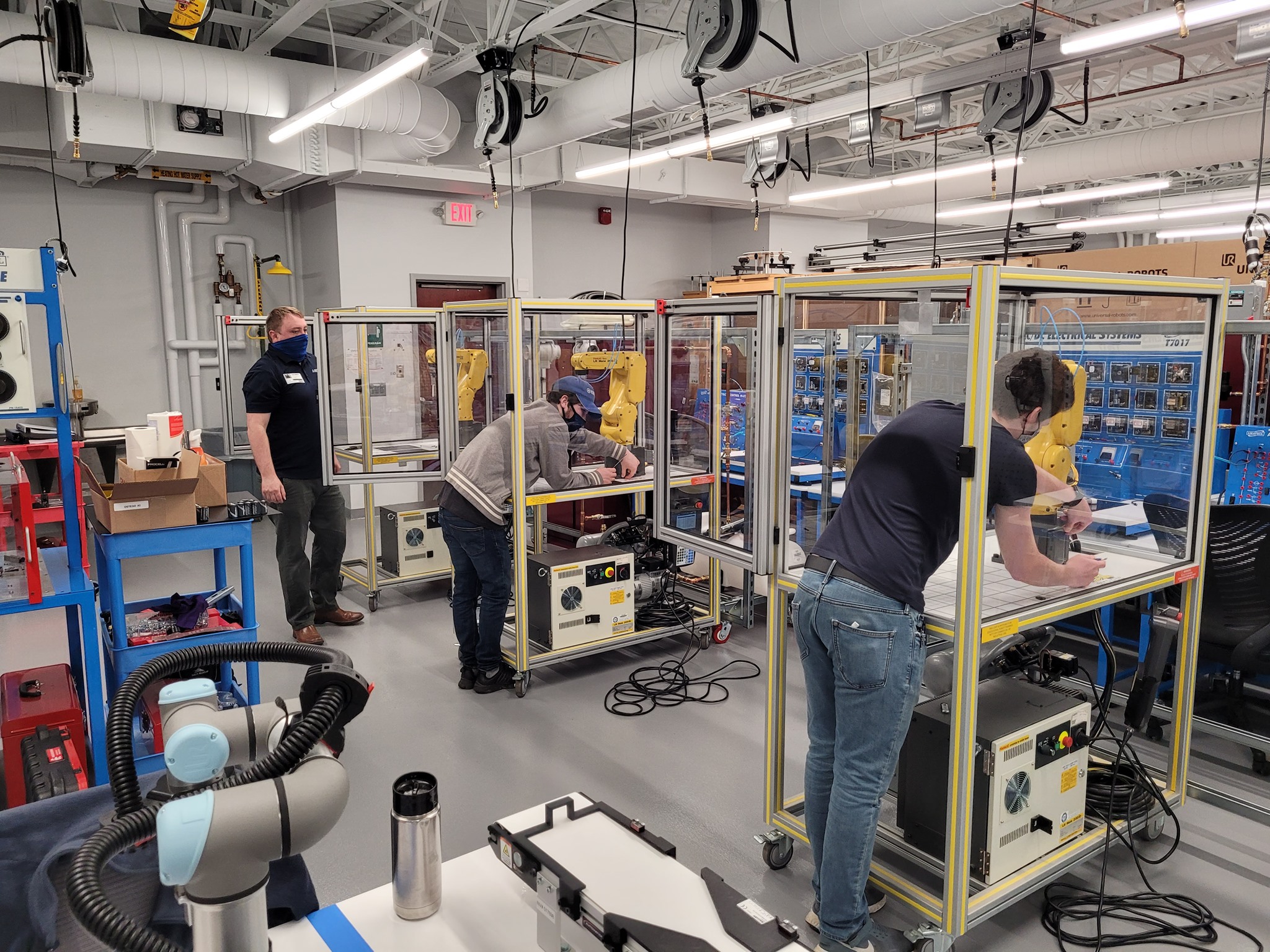 Individuals working on machinery enclosed in safety cages in a well-lit, organized workshop