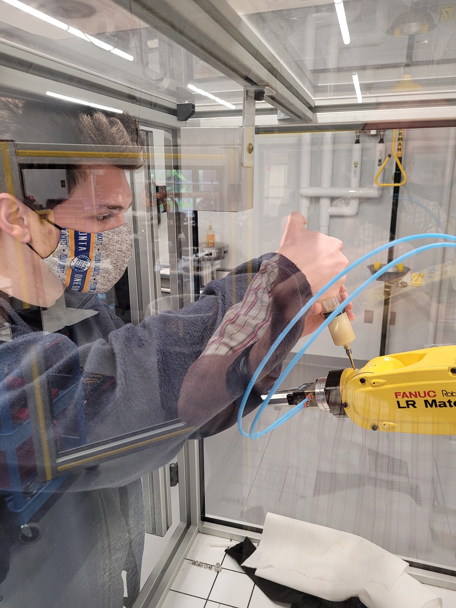 A person is interacting with a yellow robotic arm inside a glass enclosure