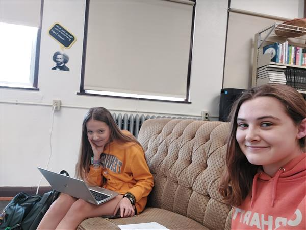 Two girls sitting on a couch with laptops, engrossed in their work and enjoying each other's company.