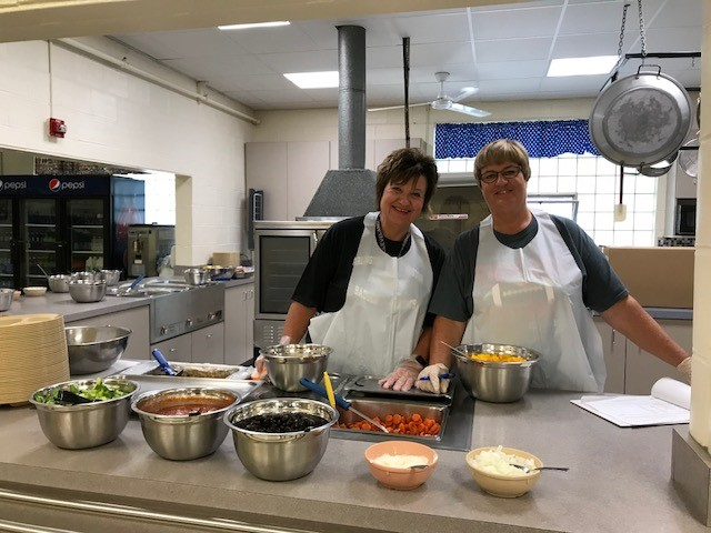 Two women in aprons smiling in a cozy kitchen.