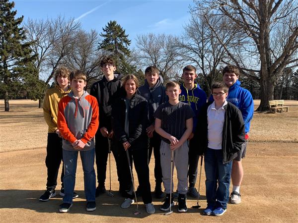 A group of young people standing on a golf course, enjoying a sunny day outdoors.