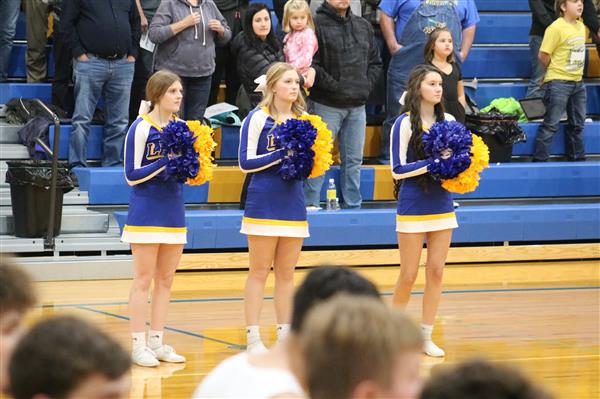 Cheerleaders in uniform, standing on basketball court, ready to perform routines during halftime show.