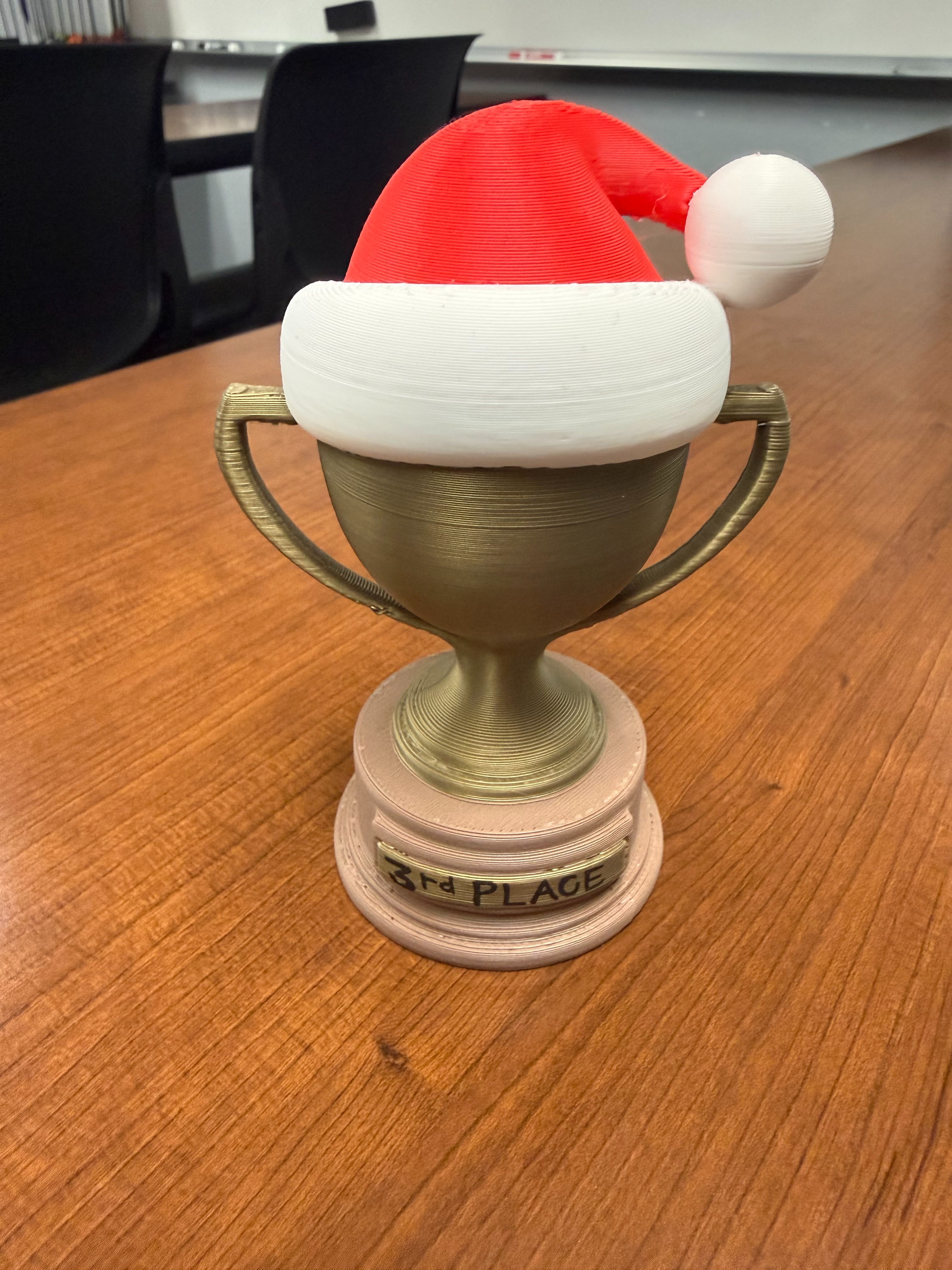 A trophy with a Santa hat on top rests on a wooden table in a room.