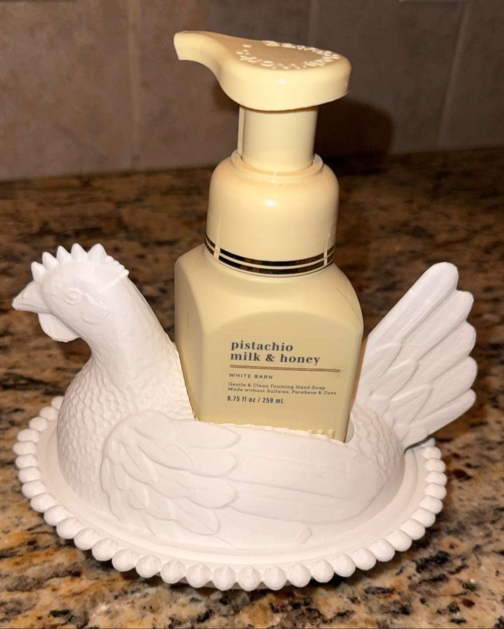 White ceramic chicken dish with a pump bottle of lotion labeled "Pistachio Milk & Honey" resting on top.