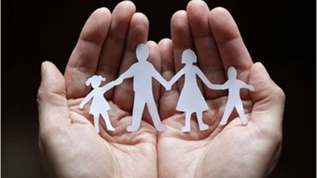 A photo of paper cutouts of people sitting on two hands while holding hands together.