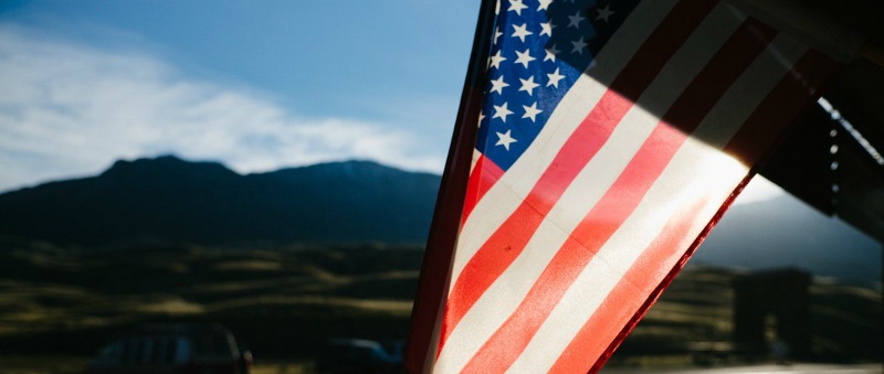 American flag displayed outdoors on a flagpole, with a mountain range visible in the distance.