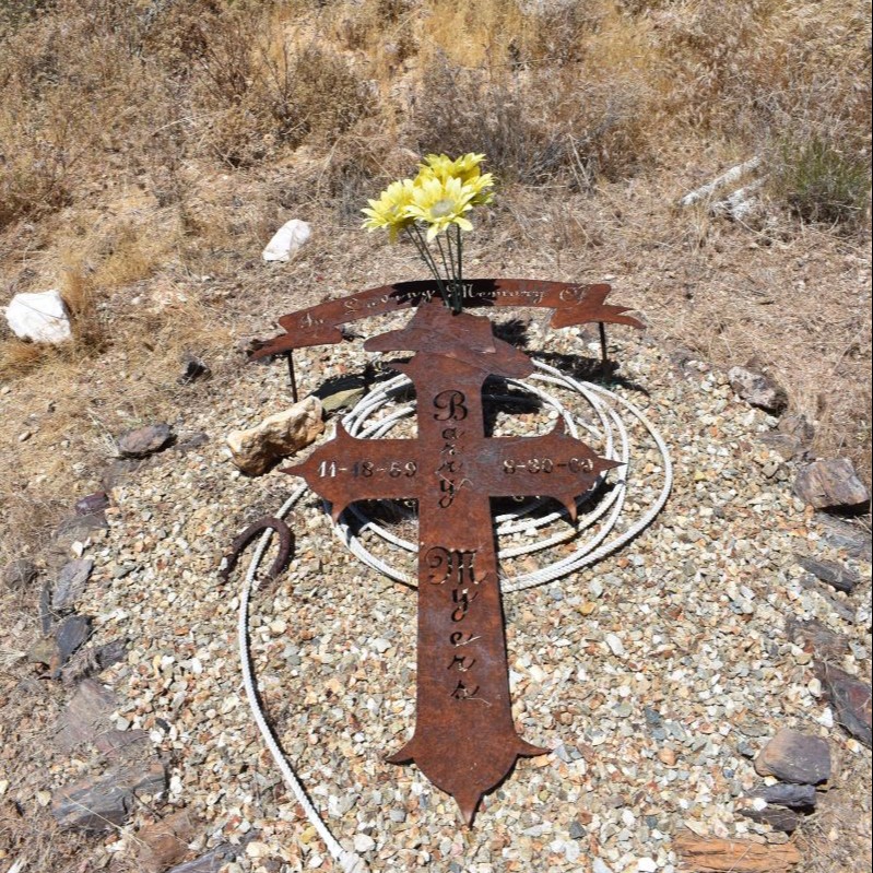 A rusty metal cross with flowers rests in the cementery.