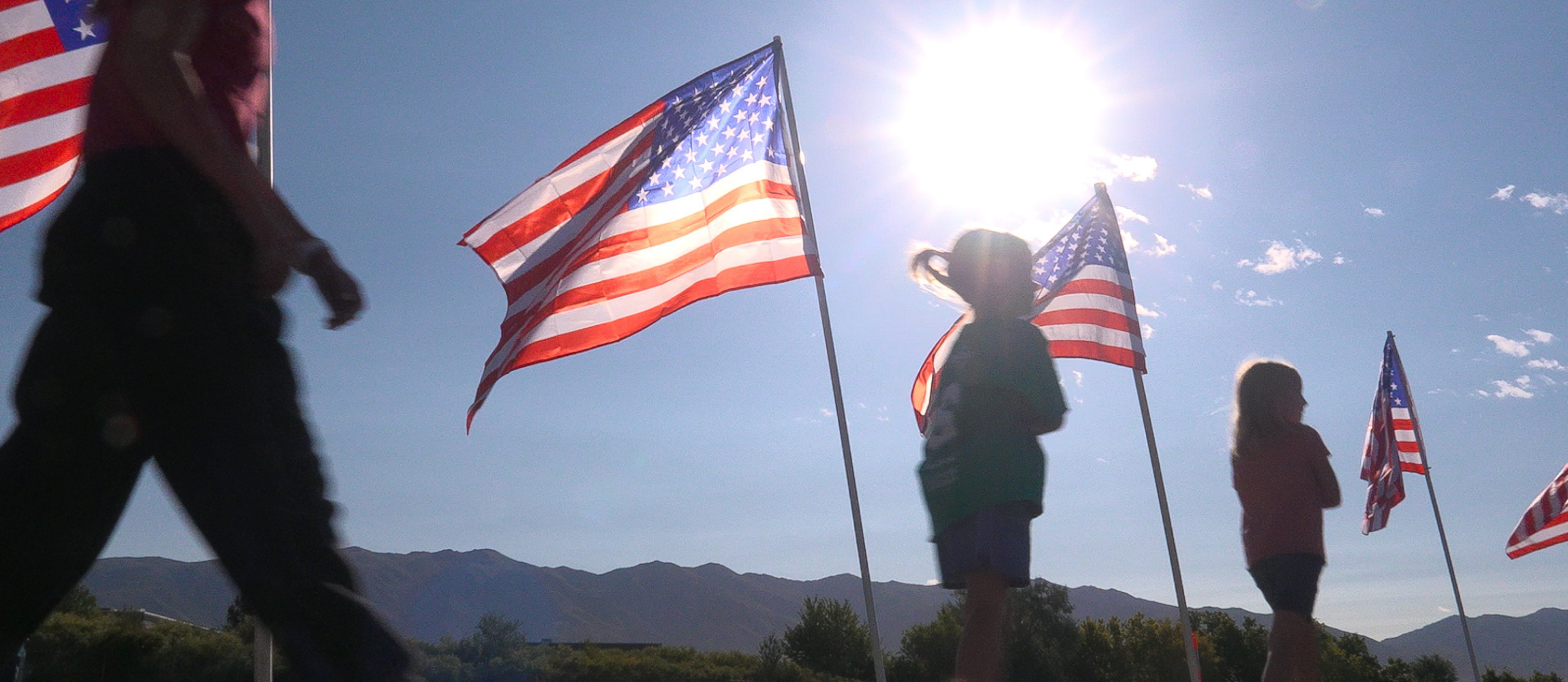 Silhouette of students walking past american flags that are glistening from the sun