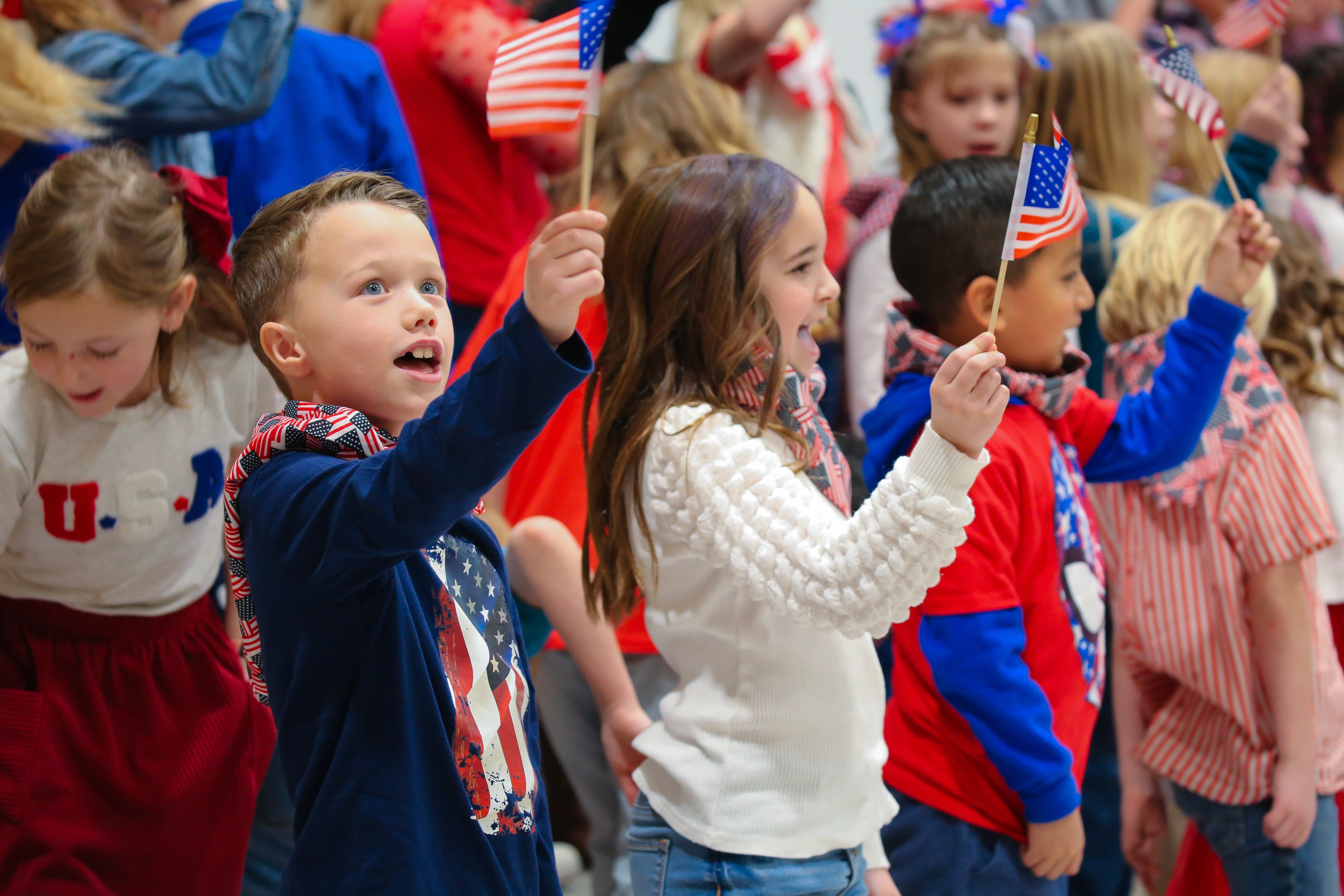 Students at West Point Elementary hold up American Flags and singing.