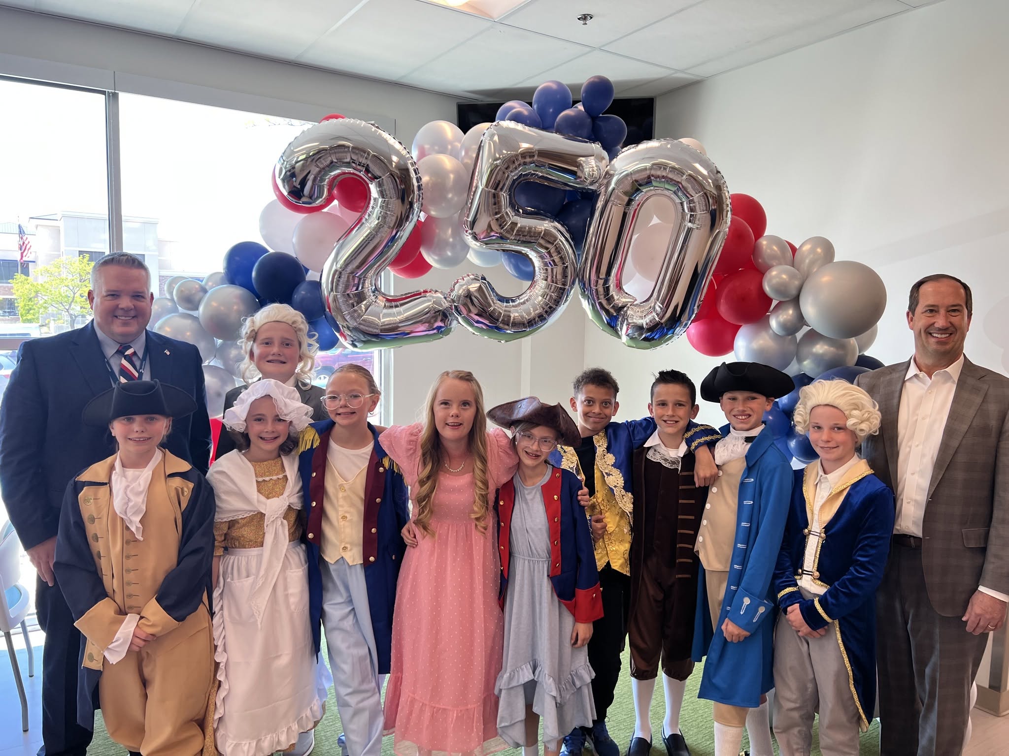 A group of students and adults standing in front of a balloon arch that has the numbers "250" in it.
