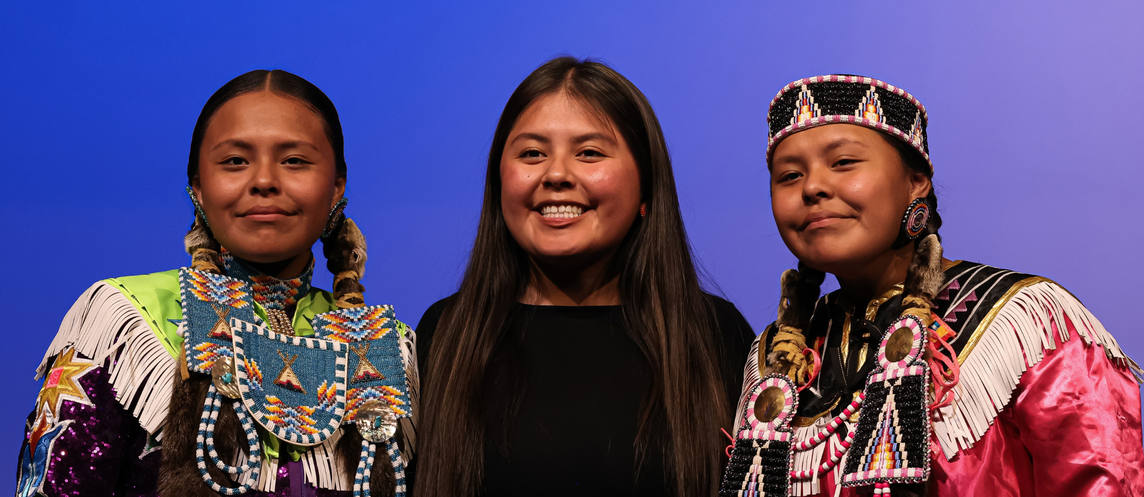 Students dressed in traditional Native American clothing stand for a photo. 