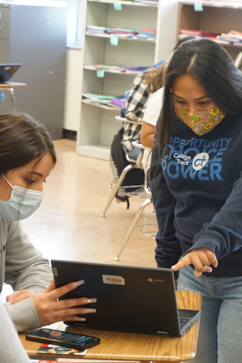 2 girls talking and using a laptop